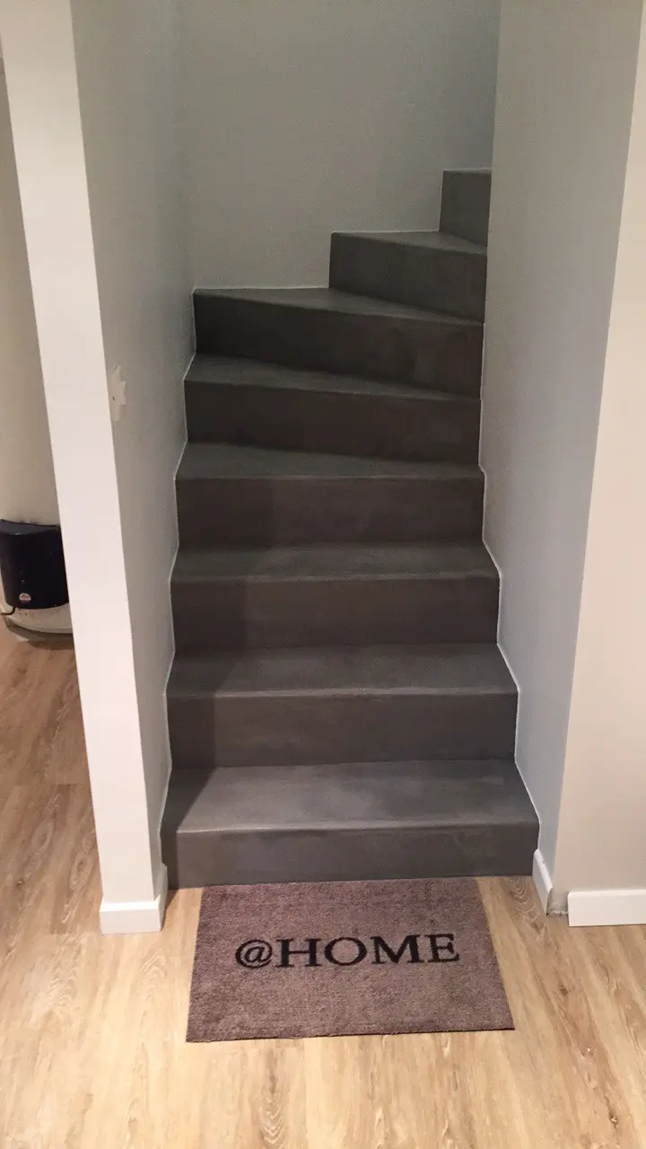 Escalier en béton ciré gris foncé, avec un enduit décoratif. Les marches sont plates et régulières, formant un escalier en colimaçon. Vue de face