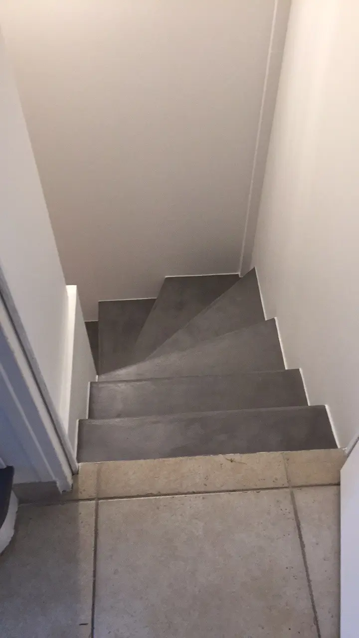 Escalier en béton ciré gris foncé, avec un enduit décoratif. Les marches sont plates et régulières, formant un escalier en colimaçon. Vue plongeante