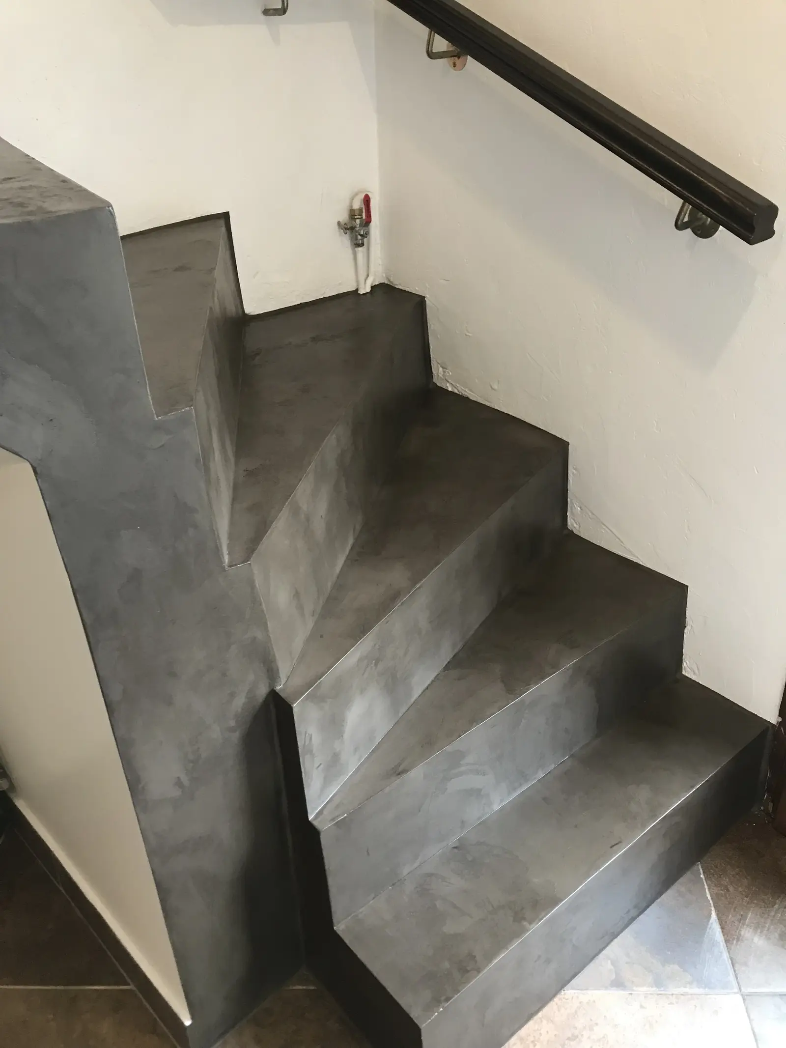 Escalier en béton ciré gris foncé, avec un enduit décoratif. Les marches sont plates et régulières, formant un escalier en colimaçon. Vue latérale