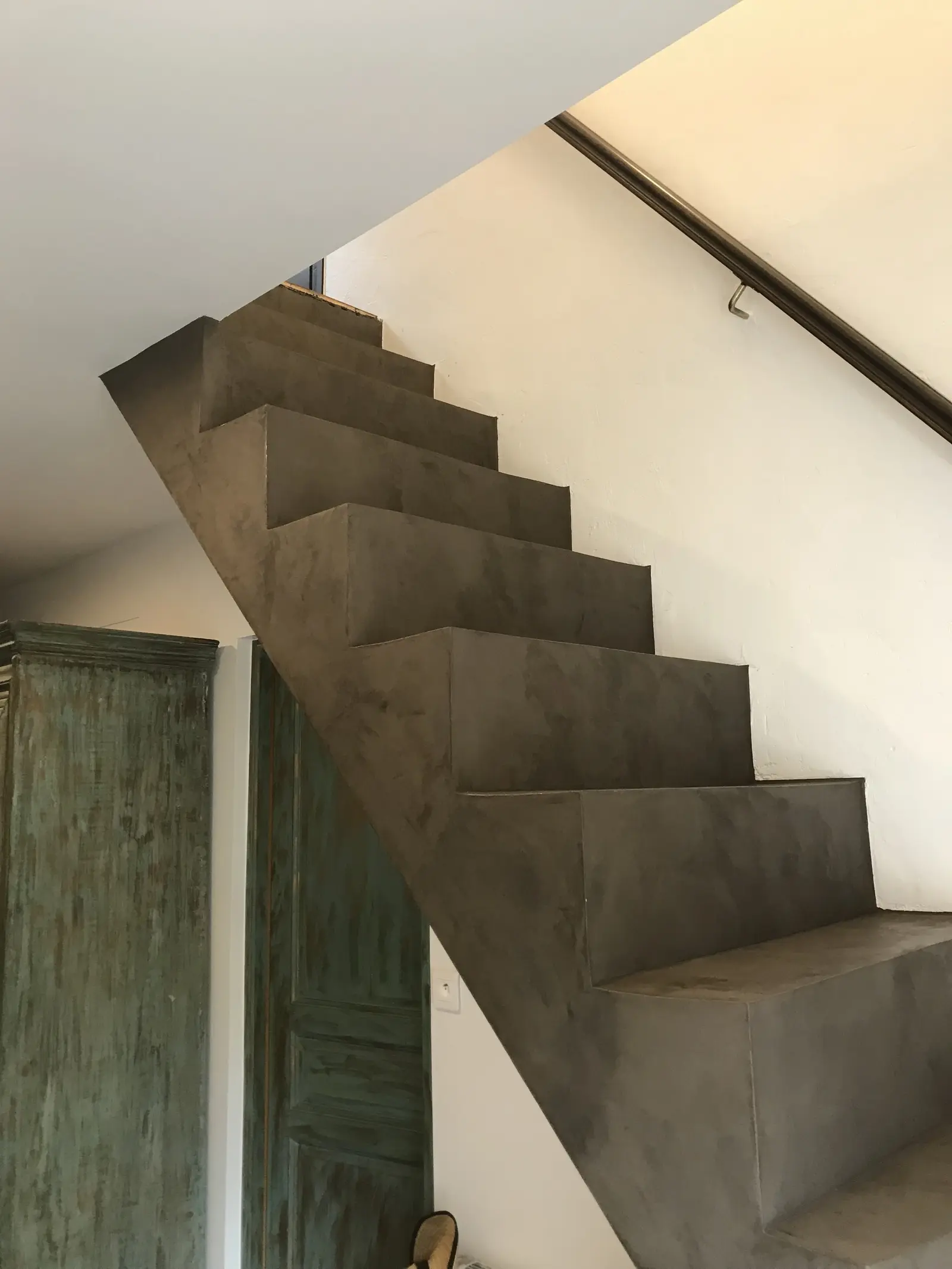 Escalier en béton décoratif, avec enduit gris foncé.  Les marches sont d'une forme géométrique. La couleur de l'enduit est uniforme et présente une légère texture.