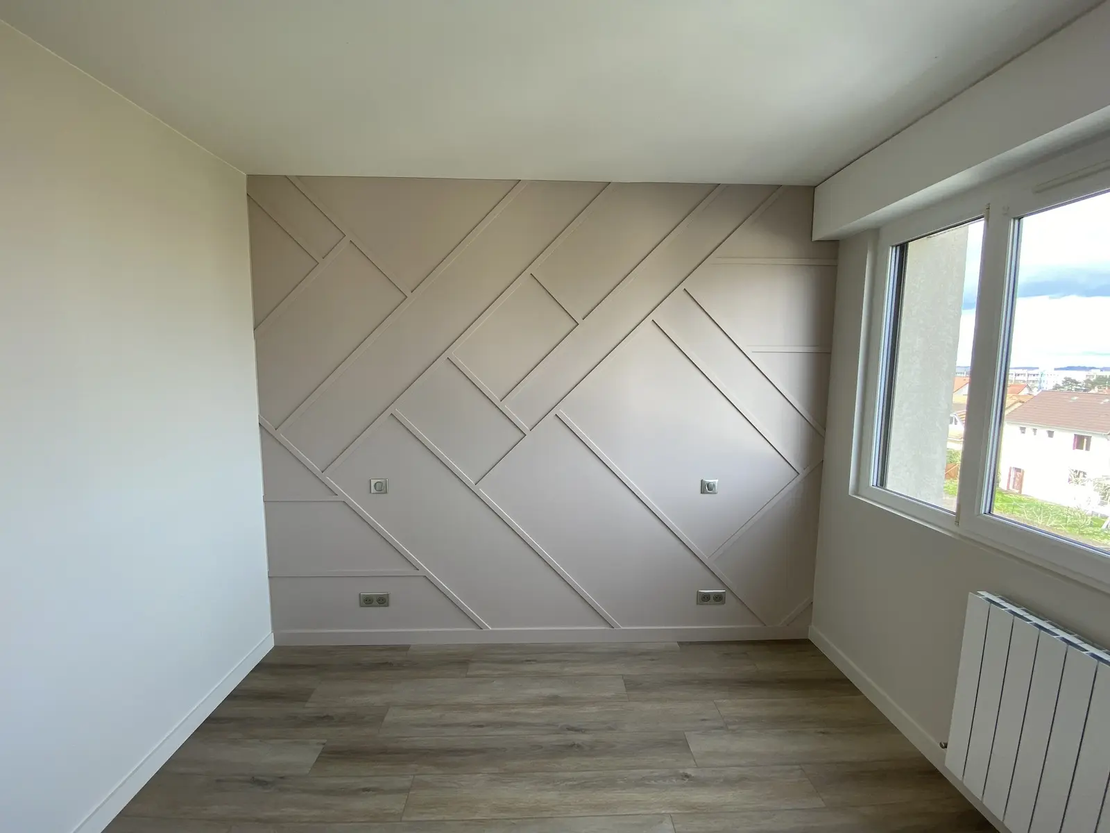 Chambre entièrement rénovée, avec un nouveau revêtement de sol et une peinture fraîche. L'un des murs se distingue par un habillage mural décoratif de couleur beige clair. Ce revêtement est composé de panneaux rectangulaires disposés en un motif géométrique qui crée une sensation de profondeur et une texture élégante à l'espace.