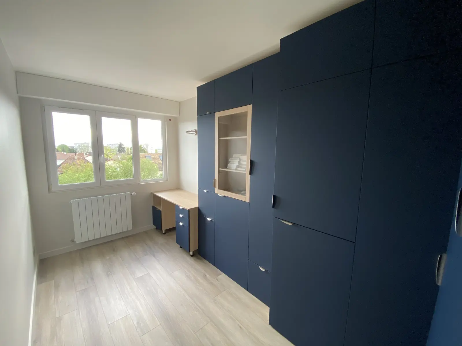 Photo d'un aménagement intérieur sur mesure. Des meubles, bleu foncé, sont intégrés dans un petit espace. On distingue un bureau, une partie armoire et un espace rangement. La disposition est optimisée selon l'espace.