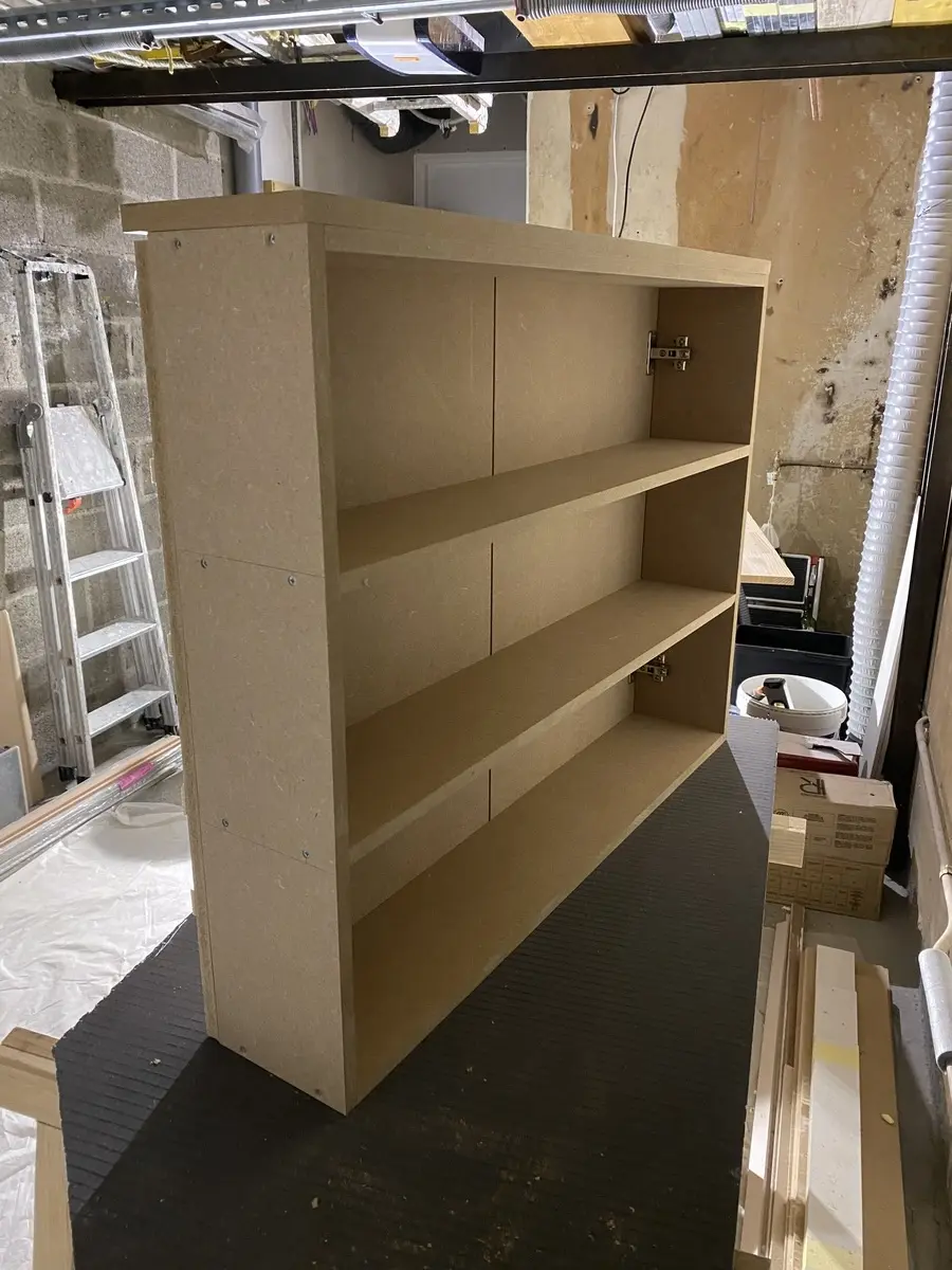 Meuble sur mesure en bois clair, en phase de construction. On aperçoit une structure à deux niveaux avec des étagères et des fixations apparentes.