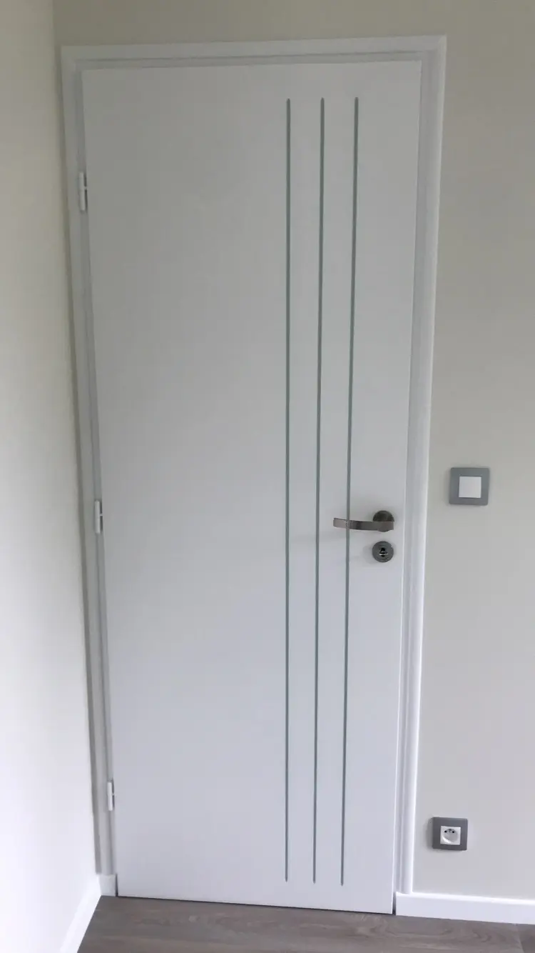 Porte intérieure blanche au rendu soigné, avec une finition de peinture uniforme et précise. Trois lignes verticales vertes, discrètement intégrées dans les rainures, apportent une touche graphique élégante.